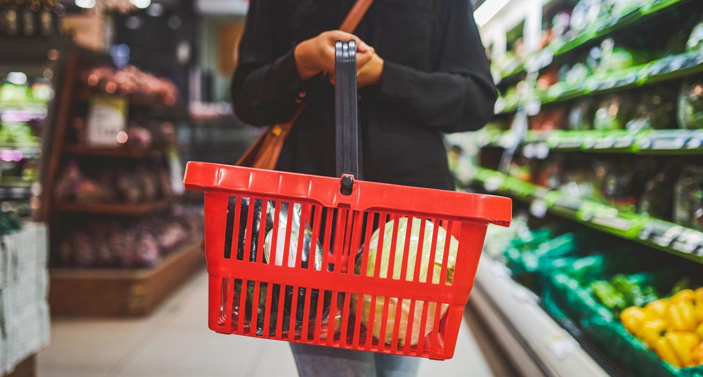 Shopper holding a red basket in a grocery store